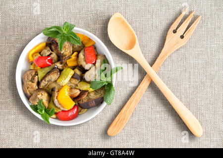 Vue de dessus d'un bol de produits frais ou grillé et légumes aubergines grillées avec salade en bois croisés sur une table beige Banque D'Images