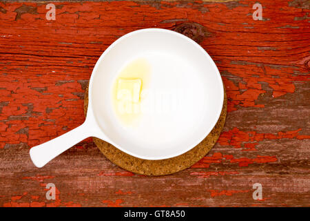 Petit morceau de beurre fondant sur une assiette blanche avec poignée sur le dessus d'une table en bois rustique, capturé en High Angle View. Banque D'Images