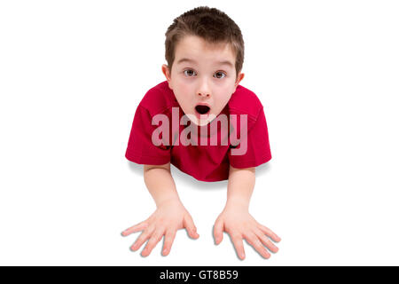 Surpris Cute Kid mâle, portant chemise rouge occasionnels, posé sur son estomac tout en regardant la caméra. Isolé sur Blanc Backgroun Banque D'Images