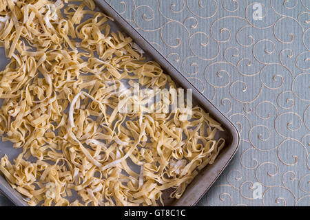 Vue aérienne de nouilles pâtes fraîches maison pâtes séchant sur un plateau de métal placé sur une nappe décorative en remuant, Banque D'Images