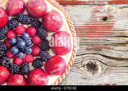 Close up Delicious Tarte fait maison avec des produits frais et Noir baies roses sur le dessus, placé sur une table en bois rustique. Capturés en haute Ang Banque D'Images