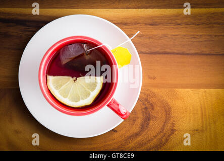 Tasse de thé fraîchement préparé à base de plantes en bonne santé avec une tranche de citron servi dans une tasse et soucoupe rouge blanc sur une table en bois avec copyspac Banque D'Images