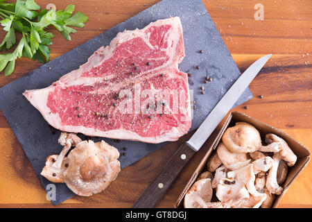 Prêt à cuire T-bone steak au poivre avec mariné sur une planche à découper, placé sur le dessus d'une table en bois avec persil et Banque D'Images