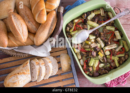Légumes frais rôti en bonne santé dans un plat allant au four, servi avec un assortiment de petits pains croustillants et dorés les tranches de pain en tant que Banque D'Images