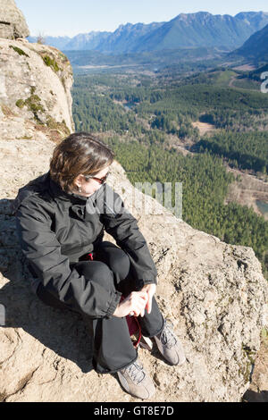 Jeune femme portant des lunettes de soleil assis sur un éperon rocheux, profitant de la vue sur la vallée boisée, le lac et les montagnes de Ratt Banque D'Images