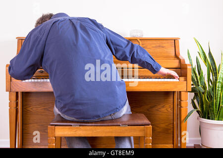Homme enthousiaste de jouer du piano avec plaisir s'étend à l'une des extrémités du clavier, vue de derrière de lui assis sur le s Banque D'Images
