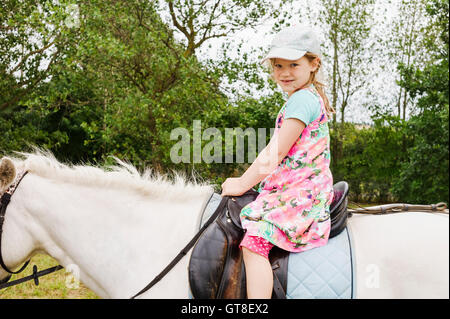 5 ans girl looking at camera tout en montant un cheval blanc, Allemagne Banque D'Images