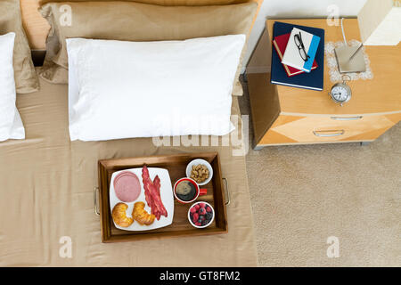 Week-end de petit-déjeuner au lit plateau sur le lit à côté de table de nuit surmontée d'une lampe, un réveil et une pile de livres Banque D'Images