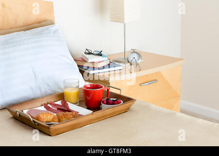 Close Up de petit-déjeuner au lit, plateau en bois avec choix de nourriture appétissante reposant sur le lit à côté de la table de chevet sont empilés avec B Banque D'Images