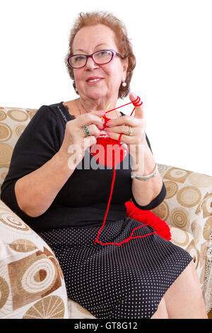 Senior lady dans une élégante robe noire portant des lunettes reposant, avec son tricot dans un fauteuil confortable, comme elle sourit à th Banque D'Images