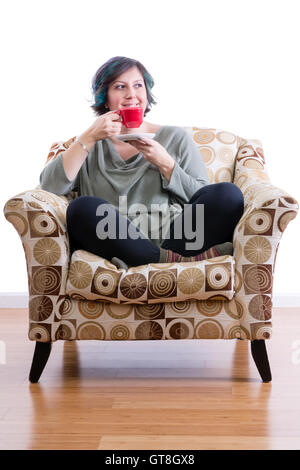 Heureuse femme d'âge moyen à la maison confortablement assis dans fauteuil appréciant son café du matin Banque D'Images