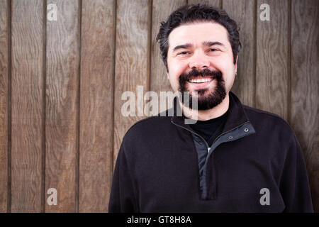 Moitié du corps d'un homme d'âge moyen avec Barbe Bouc, sincèrement Smiling at the Camera, contre un mur en bois avec l'exemplaire de l'espace. Banque D'Images