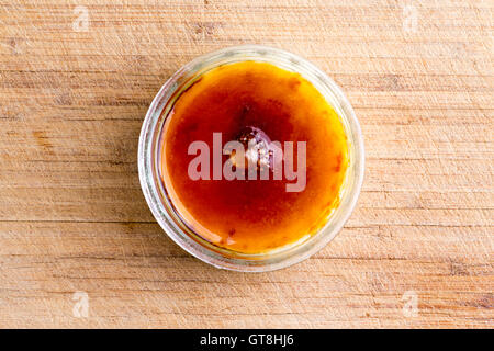 Crème brûlée croustillant garni de sucre caramélisé flambé servi dans un bol en verre vu de passage sur un conseil de bambou Banque D'Images