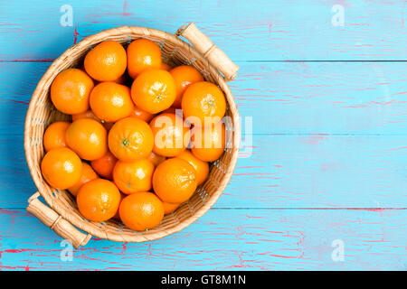 Haut première personne vue en perspective de la paille panier rempli d'oranges clémentines plus peint en bleu table en bois avec copie s Banque D'Images