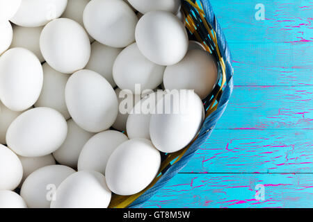 Panier en osier rempli de blanc frais de la ferme des oeufs de poules sur une table en bois peint avec peinture crackle bleu exotique with copy space Banque D'Images