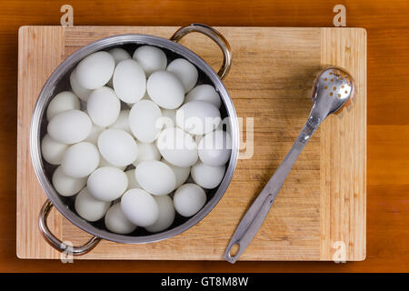 Les oeufs de poules blanc bouilli dans une casserole ou dans une passoire métallique debout sur une planche en bois pour la décoration de refroidissement avec du colorant de couleur pour th Banque D'Images