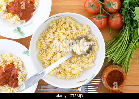 Vue de haut en bas les pâtes rotini cuits et cuillère en acier inoxydable dans un bol sur la table à côté a servi les plaques, les tomates, le persil Banque D'Images