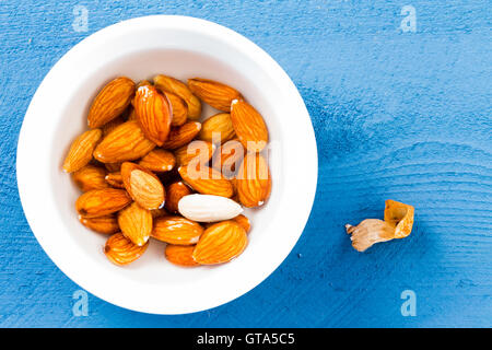 Bol d'amandes brutes fraîches pelées avec un contre un fond bleu vu depuis une vue de dessus Banque D'Images