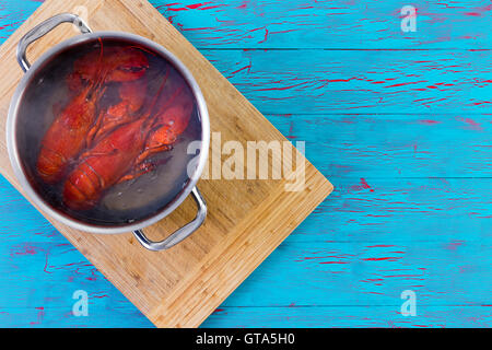 Deux tout fraîchement bouillie rouge coloré les homards dans un pot d'eau debout sur une planche à découper en bambou sur un crépitement bleu p Banque D'Images