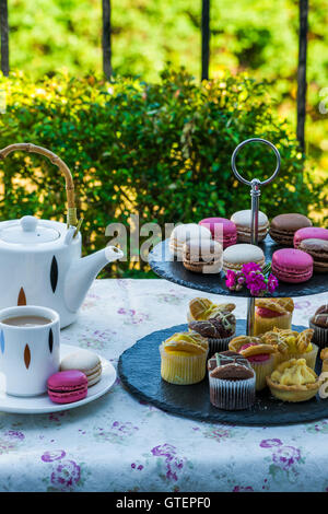 Un thé avec gâteaux et macarons mis en place sur la table dans le jardin Banque D'Images