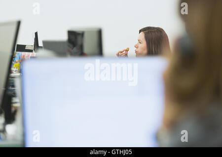 Businesswoman eating et working at desk in office Banque D'Images