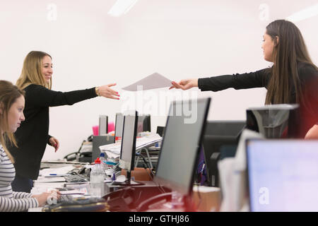 Businesswoman handing paperwork à collègue sur ordinateurs de bureau Banque D'Images