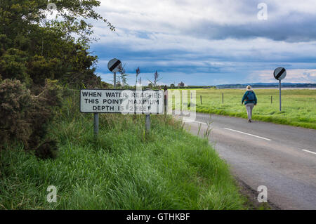 Un marcheur passant un raz-de-crue panneau sur la route en Bowness-on Solway, Cumbria, Angleterre Banque D'Images