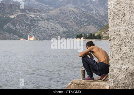 Baie de Kotor, Monténégro - Skinny homme accroupi sur le bord de la relève l'îlot Notre-Dame de la Gospa od Skrpjela (roches) Banque D'Images