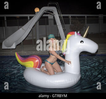 Orange County, Californie, USA. 3e, 2016 Sep. Une jolie jeune femme blonde portant un bikini et trucker cap se trouve sur un inflaitable licorne flottant dans une piscine la nuit. © David Bro/ZUMA/Alamy Fil Live News Banque D'Images