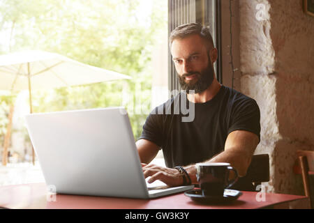 Handsome Businessman Wearing Barbu Tshirt noir pour ordinateur portable Table de travail bois urbains Cafe.Jeune Manager Portable Travail Design intérieur moderne Place.Processus Coworking Business Startup.arrière-plan flou. Banque D'Images