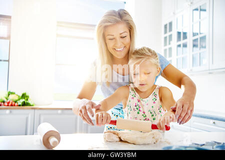 Cute little girl apprendre à abaisser la pâte qu'elle aide sa mère dans la cuisine avec la cuisson , high key with copy space Banque D'Images