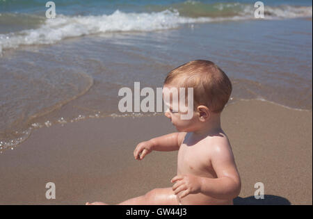 Happy Baby garçon assis sur le sable et l'observation de la mer sur la plage Banque D'Images