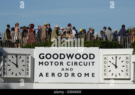 Le Goodwood Revival. Le circuit du moteur et de l'Aérodrome de Goodwood signe avec des horloges. Vintage d'époque avec des gens en costume d'époque Banque D'Images