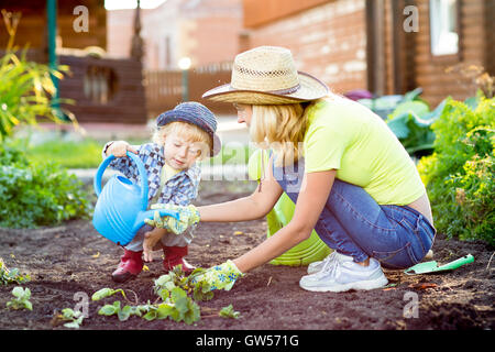 Garçon enfant contribue à mère travaillant dans le jardin Banque D'Images