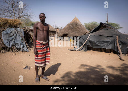 Grand homme de la tribu Karo dans son village dans la vallée de l'Omo d'Ethiopie avec huttes au toit de chaume dans l'arrière-plan Banque D'Images