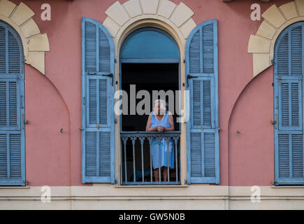 Femme plus âgée s'appuie sur le balcon d'un immeuble élégant avec ses volets aux portes et ouvertures Banque D'Images