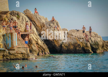 Les jeunes garçons dive off une plate-forme dans les eaux bleues de la mer Méditerranée tandis que d'autres regardent et attendent leur tour Banque D'Images