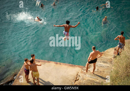 Les jeunes garçons dive off une plate-forme dans les eaux bleues de la mer Méditerranée tandis que les nageurs regardez ci-dessous Banque D'Images