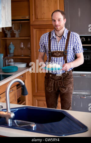 L'homme dans des vêtements traditionnels bavarois debout dans cuisine avec une assiette d'œufs et smiling at camera Banque D'Images