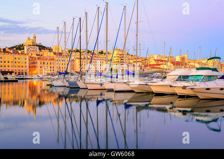 Yachts blancs se reflétant dans les rangs de l'eau encore de l'ancien Vieux Port de Marseille avec Notre Dame de Paris, en France, le sunr Banque D'Images