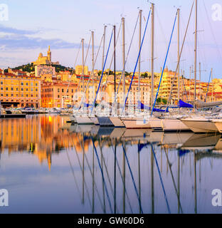 Yachts blancs se reflétant dans les rangs de l'eau encore de l'ancien Vieux Port de Marseille avec Notre Dame de Paris, en France, le sunr Banque D'Images