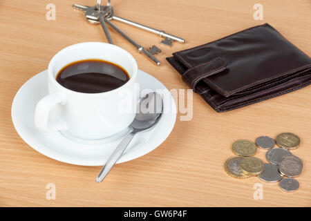 Tasse de café noir sur une table en bois avec un porte-monnaie, monnaie et un jeu de clés Banque D'Images