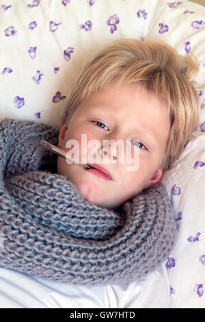 Sick little boy holding pose thermomètre au lit avec visage triste - santé et médecine concept Banque D'Images