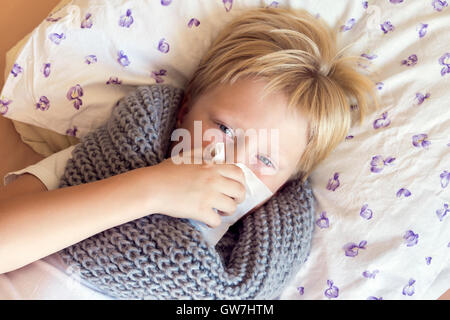 Petit enfant malade boy blowing nose fixant au lit avec visage triste - santé et médecine concept Banque D'Images