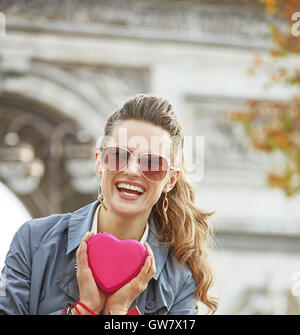 Saint-valentin élégant à Paris. Portrait of happy trendy woman in sunglasses with shopping bags près de l'Arc de Triomphe à Paris, France montrant red boîte de chocolats en forme de coeur Banque D'Images