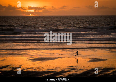 Une femme vu en silhouette alors qu'elle s'étend le long de la plage de Fistral, Newquay en Cornouailles.. Banque D'Images