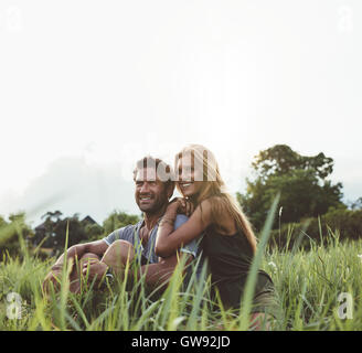 Loving young couple sitting on grass field. L'homme et la femme profitant moment romantique en plein air dans le pré. Banque D'Images
