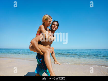 Vue de côté coup de jeune homme s'occuper sa petite amie sur le dos à la plage. Couple sur le dos au bord de la mer. Banque D'Images