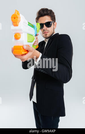 L'accent d'affaires en costume et lunettes de tir avec canon à eau sur fond gris Banque D'Images