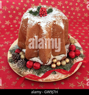 Gâteau de noël Pandoro avec Holly, sucre glace dépoussiérage, décorations babiole sur une étoile rouge et or contexte. Banque D'Images